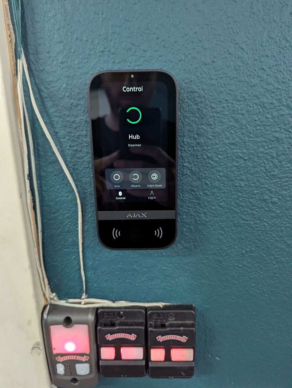 An Ajax touchscreen keypad on a teal wall showing the hub disarmed, with arm, disarm and night mode buttons