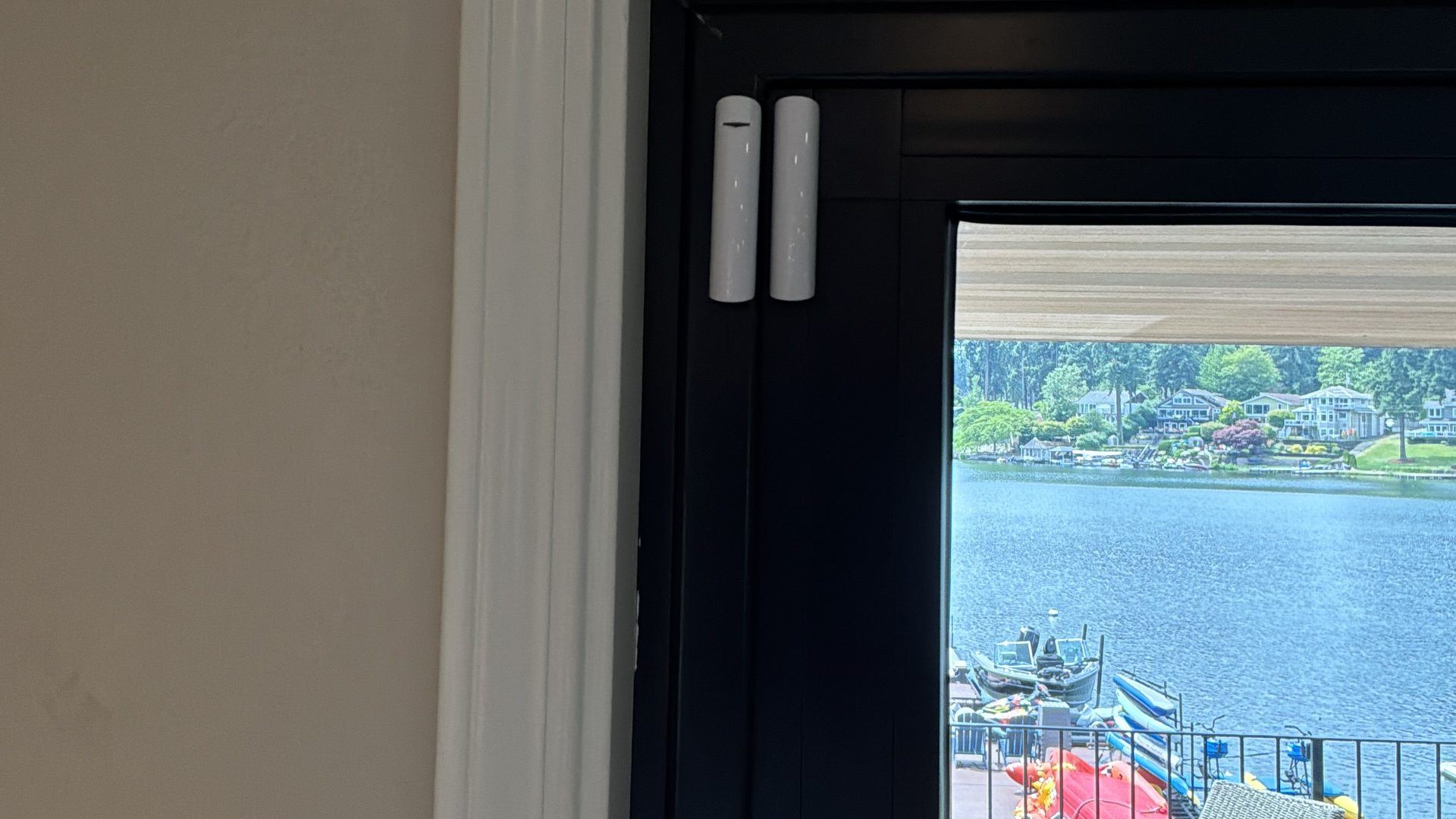 A white Ajax DoorProtect contact on a black sliding door frame in a Tacoma home, with the lake and a dock beyond
