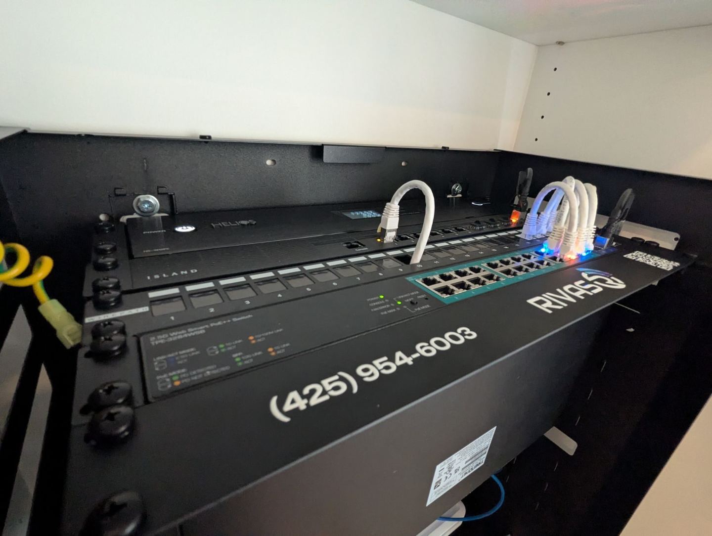 The finished wall rack in a Tacoma home: an Island Router Pro above a TRENDnet 2.5G PoE++ switch on a panel marked Rivas Technology Group