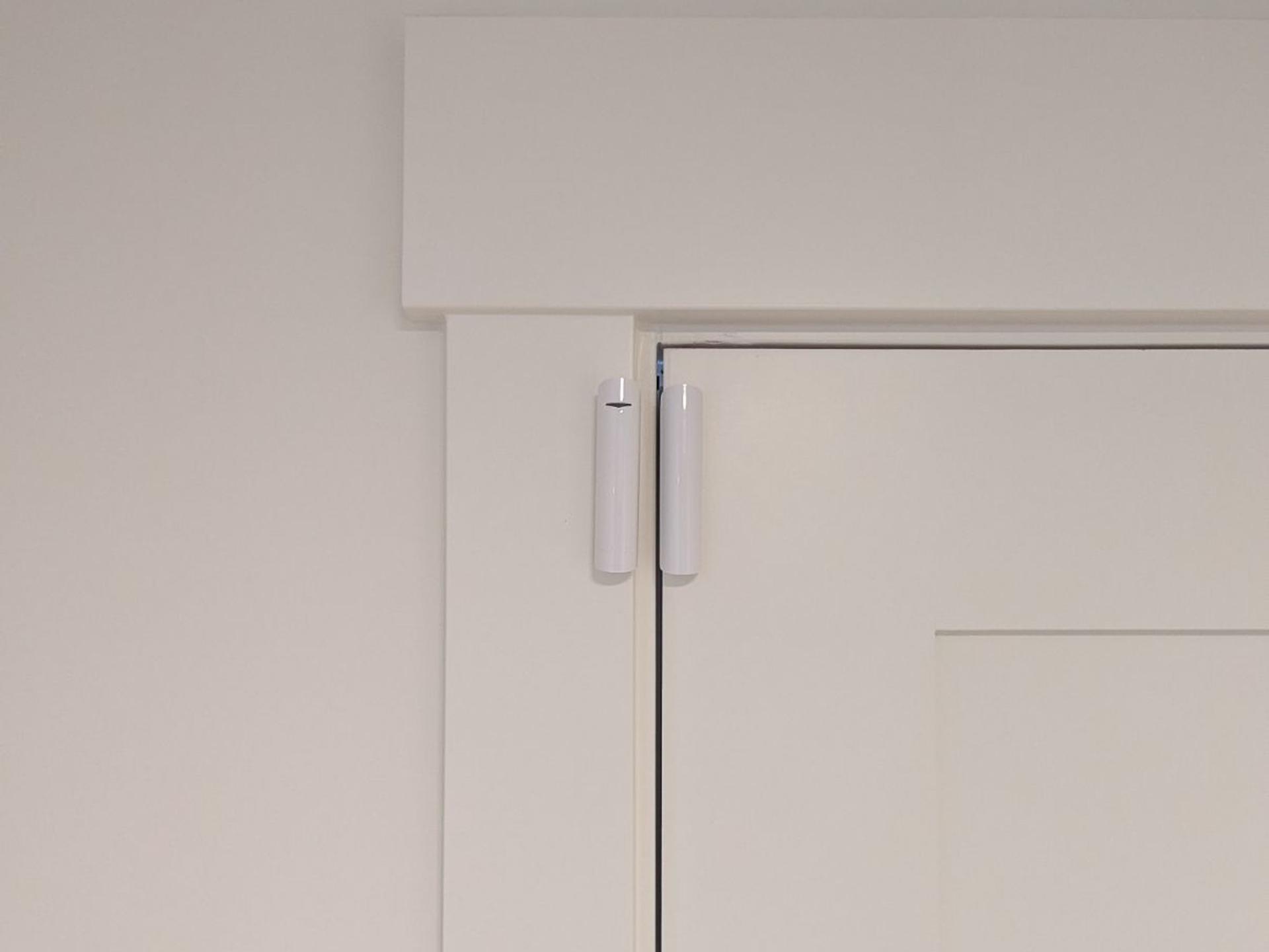 A white Ajax DoorProtect sensor at the top corner of a white painted door frame