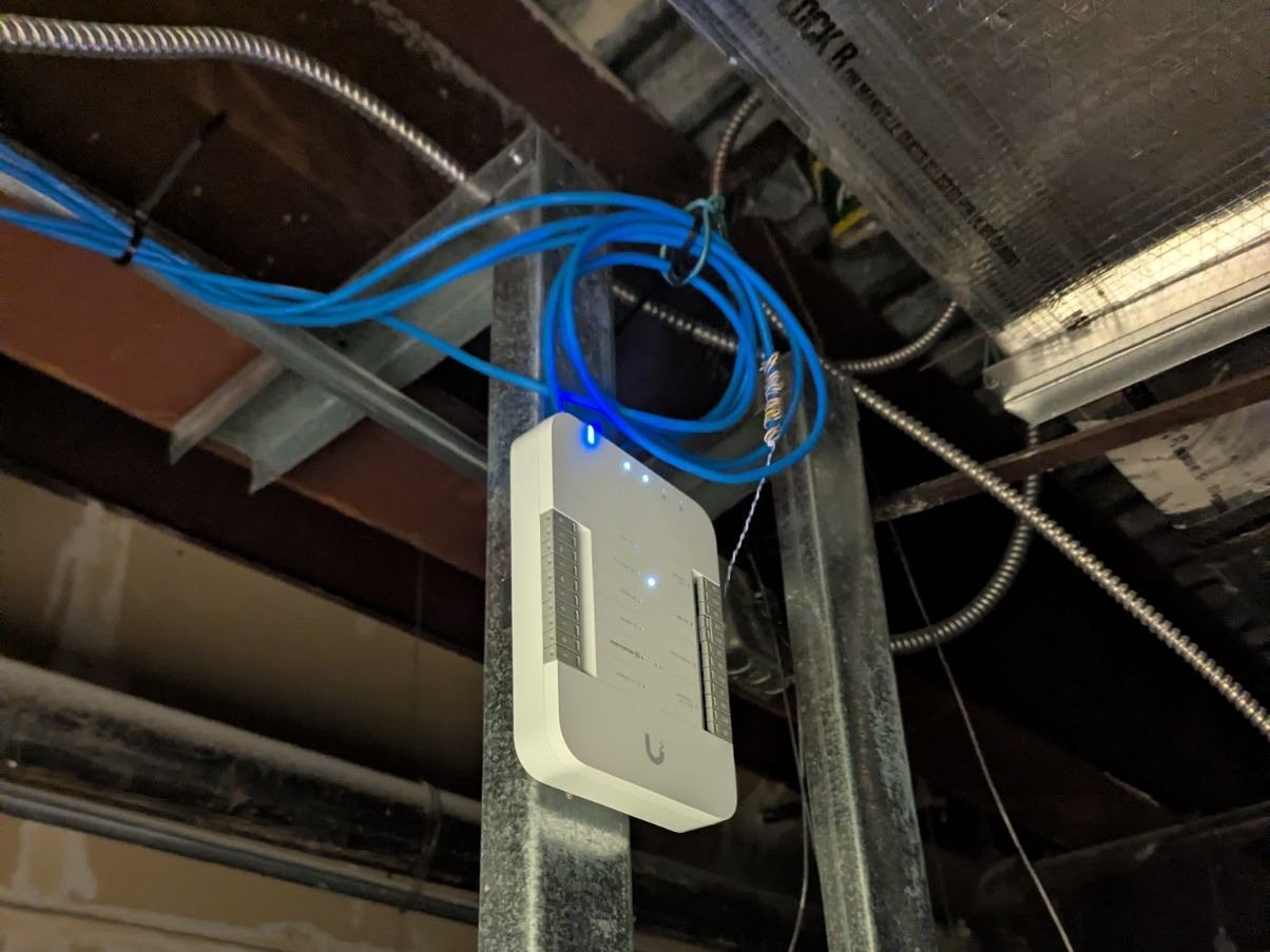 A UniFi Access Hub mounted on strut above the ceiling of the Bellevue office, with blue Ethernet runs to it