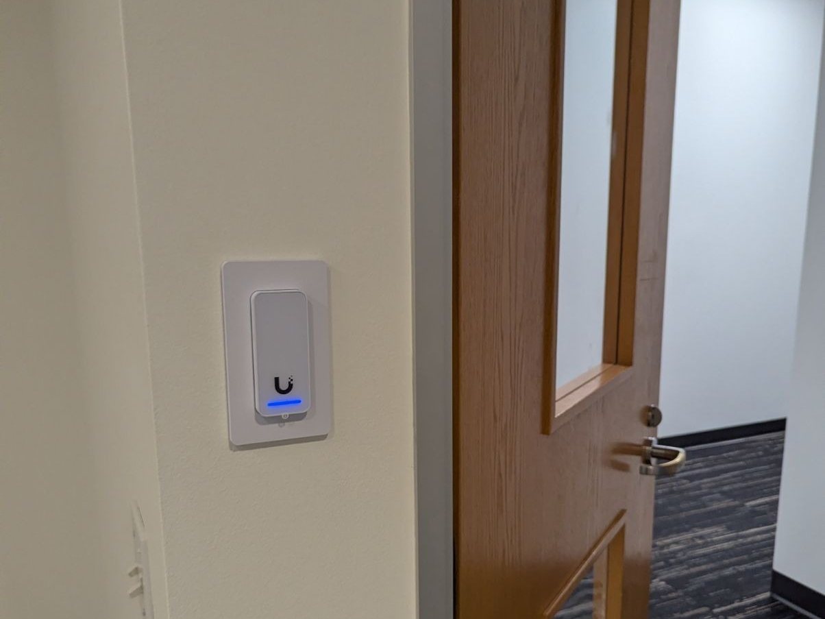 A compact UniFi Access NFC reader beside a wood office door