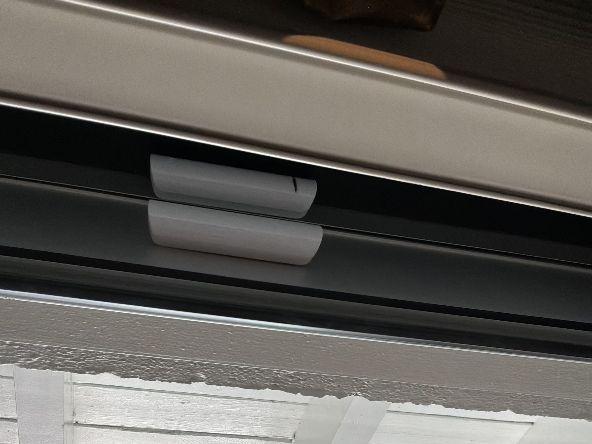 A white Ajax DoorProtect contact on the header of a black patio door under a white-painted covered porch