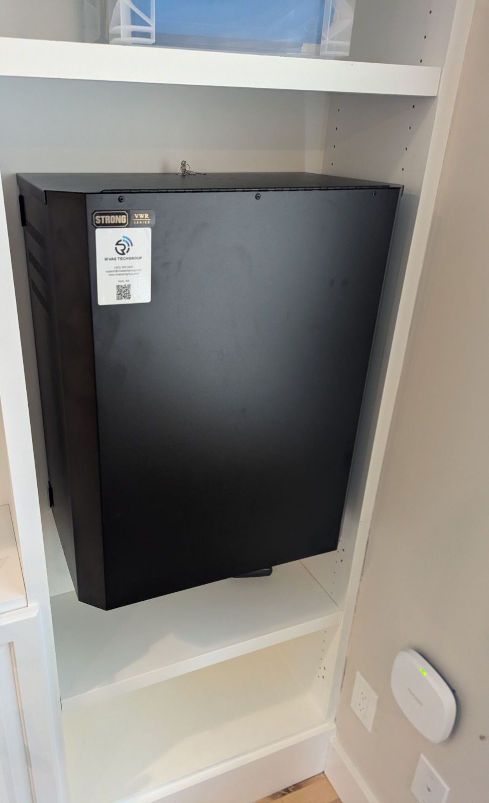 The closed black Strong wall rack inside white built-in shelving, with a Rivas Technology Group support label on the door